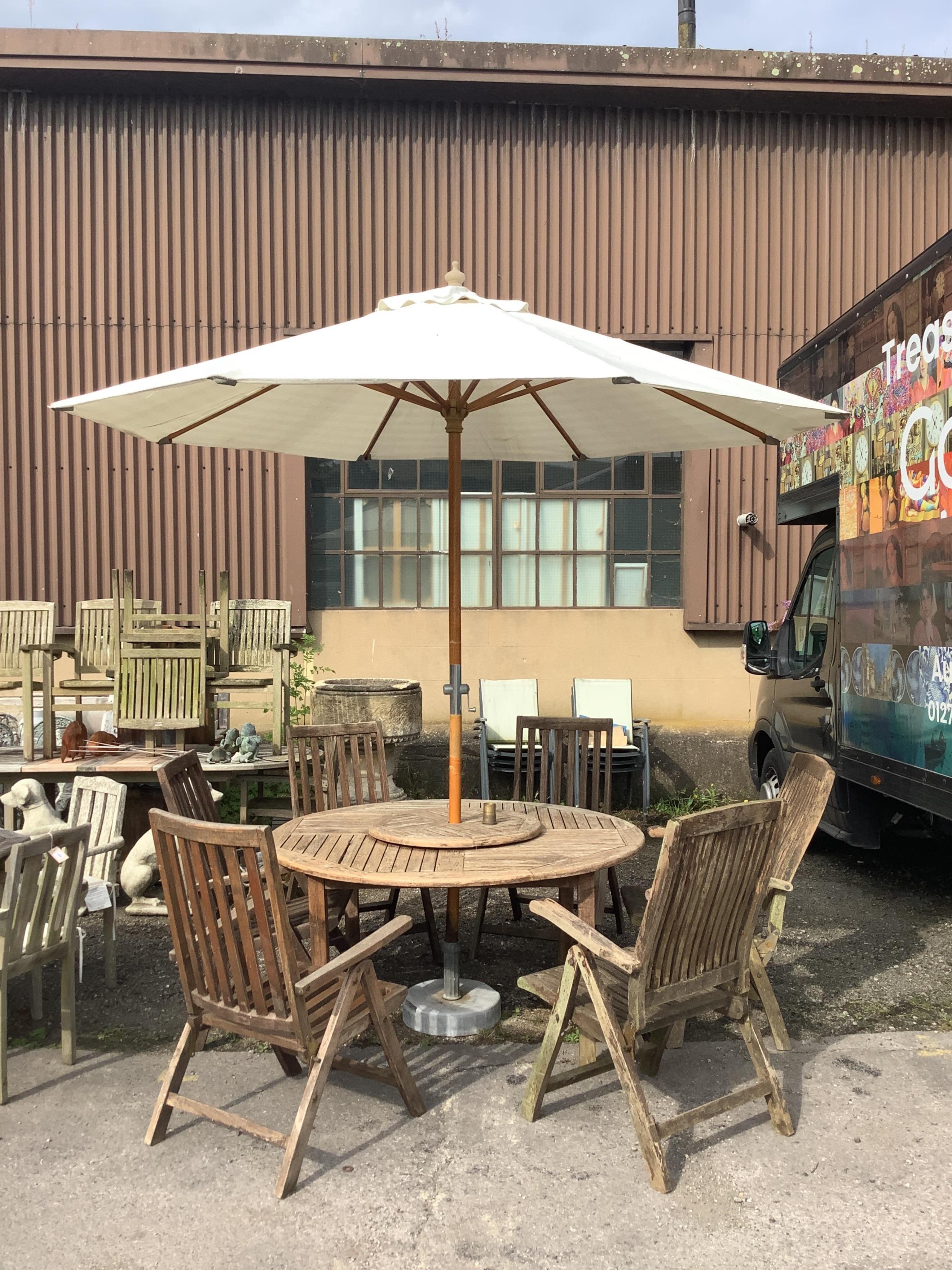 A circular weathered teak garden table with lazy Susan, diameter 150cm, height 75cm, a crank parasol and six (four plus two) folding armchairs. Condition - fair